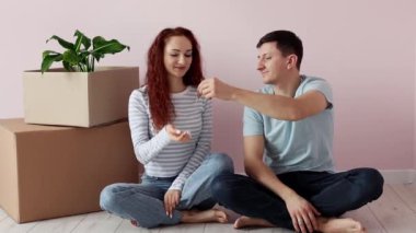 Genç ve mutlu bir çift yerde karton kutuların yanında oturuyor, koca kameraya bir sürü anahtar gösteriyor. Yeni ev. Yeni bir evin sembolü. Gayrimenkul ve kiracılık, kredi ve ipotek, taşınma