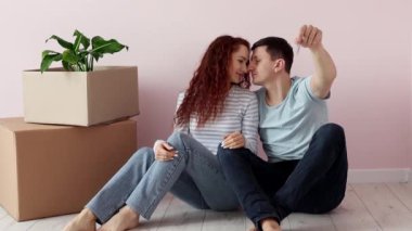 Genç ve mutlu bir çift yerde karton kutuların yanında oturuyor, koca kameraya bir sürü anahtar gösteriyor. Yeni ev. Yeni bir evin sembolü. Gayrimenkul ve kiracılık, kredi ve ipotek, taşınma