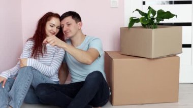 Genç ve mutlu bir çift yerde karton kutuların yanında oturuyor, koca kameraya bir sürü anahtar gösteriyor. Yeni ev. Yeni bir evin sembolü. Gayrimenkul ve kiracılık, kredi ve ipotek, taşınma