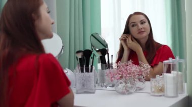 Gece elbisesi giyen bir kız parfüm sıkar. Makyaj yapan genç ve çekici bir kadın tuvalet masasının arkasında ağır çekimde.