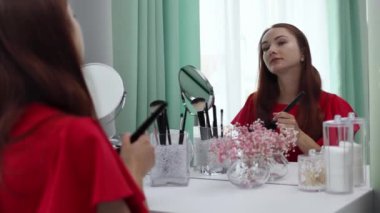 Gece elbisesi giymiş bir kız yüzüne pudra sürer. Genç ve çekici bir kadın makyaj yapıyor. Tuvalet masasının arkasında..