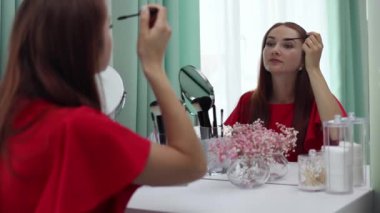 Gece elbisesi giymiş bir kız kirpiklerine rimel sürer. Genç ve çekici bir kadın makyaj yapıyor. Tuvalet masasının arkasında..