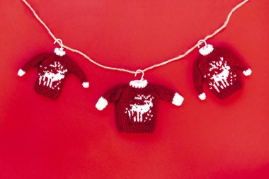 Kırmızı arka planda izole edilmiş, üzerinde geyik resmi olan kırmızı kazaklar örülmüş. Noel ve Yeni Yıl atmosferi. Noel afişi, maket.