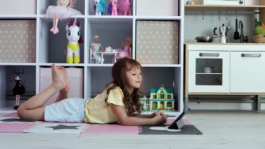 Avrupa görünümlü küçük bir kız ağır çekimde tablet kullanıyor. Çocuk sanal oyunlar oynuyor ya da tabletinde çizgi film izliyor. Tabletli çocuk. Alet bağımlılığı sorunu. 4k görüntü.
