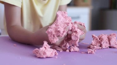 Çocuk kinetik kumla oynuyor ve yavaş çekimde elinde karıştırıyor. Pembe kinetik anti-stres kumu olan çocukların ellerine yakından bakın. Çocuklar ve yetişkinler için stres önleyici oyuncak.
