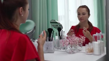 Gece elbisesi giyen bir kız parfüm sıkar. Makyaj yapan genç ve çekici bir kadın tuvalet masasının arkasında ağır çekimde.