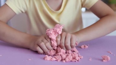 Çocuk kinetik kumla oynuyor ve yavaş çekimde elinde karıştırıyor. Pembe kinetik anti-stres kumu olan çocukların ellerine yakından bakın. Çocuklar ve yetişkinler için stres önleyici oyuncak.