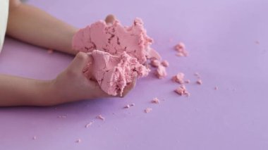 Çocuk kinetik kumla oynuyor ve yavaş çekimde elinde karıştırıyor. Pembe kinetik anti-stres kumu olan çocukların ellerine yakından bakın. Çocuklar ve yetişkinler için stres önleyici oyuncak.