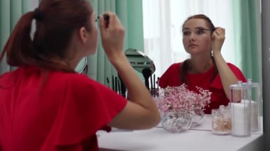 Gece elbisesi giymiş bir kız kirpiklerine rimel sürer. Genç ve çekici bir kadın makyaj yapıyor. Tuvalet masasının arkasında..