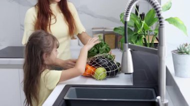 Anne ve kızı organik sebzeleri ve meyveleri modern mutfakta ağır çekimde çıkarıyorlar. Market alışverişi. Sıfır israf. Eko-Arkadaş Alışverişi. Sağlıklı yaşam tarzı kavramı.