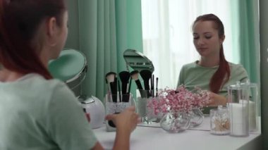 Genç bir kadın aynaya yavaş çekimde bakarken yüzüne krem sürüyor. Cilt bakımı. Güzellik anlayışı, kişisel bakım ve günlük krem kullanımı.