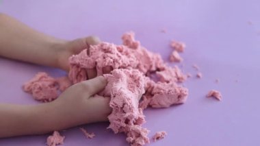 Çocuk kinetik kumla oynuyor ve yavaş çekimde elinde karıştırıyor. Pembe kinetik anti-stres kumu olan çocukların ellerine yakından bakın. Çocuklar ve yetişkinler için stres önleyici oyuncak.