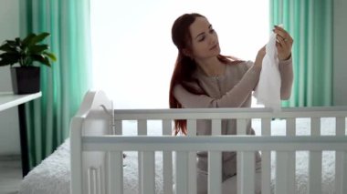 Yeni doğmuş bir bebeğe bakma kavramı. Avrupa görünümlü genç bir anne beşiğinde yatan yeni doğmuş bir bebekle oynuyor. Annem doğum izninde. Annelik kavramı. Yavaş çekim.