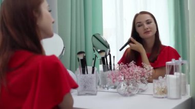 Gece elbisesi giymiş bir kız yüzüne pudra sürer. Genç ve çekici bir kadın makyaj yapıyor. Tuvalet masasının arkasında..