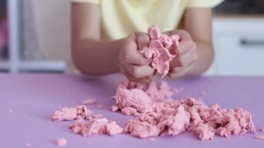 Çocuk kinetik kumla oynuyor ve yavaş çekimde elinde karıştırıyor. Pembe kinetik anti-stres kumu olan çocukların ellerine yakından bakın. Çocuklar ve yetişkinler için stres önleyici oyuncak.
