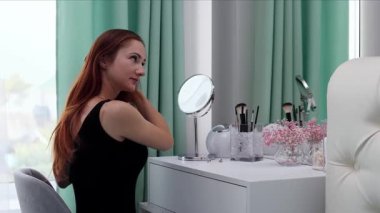 Gece elbisesi giymiş bir kız saçını tarıyor. Makyaj yapan genç ve çekici bir kadın tuvalet masasının arkasında ağır çekimde.