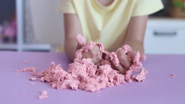 Çocuk elinde karıştırarak kinetik kumla oynuyor. Pembe kinetik anti-stres kumu olan çocukların ellerine yakından bakın. Çocuklar ve yetişkinler için stres önleyici oyuncak. 4k görüntü.