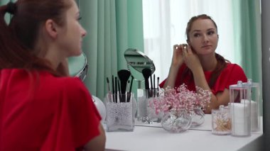 Gece elbisesi giymiş bir kız küpe takıyor. Makyaj yapan genç ve çekici bir kadın tuvalet masasının arkasında ağır çekimde