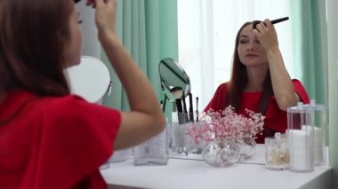 Gece elbisesi giymiş bir kız yüzüne pudra sürer. Genç ve çekici bir kadın makyaj yapıyor. Tuvalet masasının arkasında..