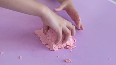 Çocuk kinetik kumla oynuyor ve yavaş çekimde elinde karıştırıyor. Pembe kinetik anti-stres kumu olan çocukların ellerine yakından bakın. Çocuklar ve yetişkinler için stres önleyici oyuncak.