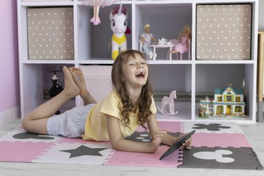 Tablet kullanan Avrupalı görünümlü küçük bir kız. Çocuk sanal oyunlar oynuyor ya da tabletinde çizgi film izliyor. Tabletli çocuk. Alet bağımlılığı sorunu..