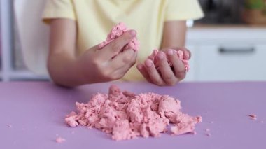 Çocuk kinetik kumla oynuyor ve yavaş çekimde elinde karıştırıyor. Pembe kinetik anti-stres kumu olan çocukların ellerine yakından bakın. Çocuklar ve yetişkinler için stres önleyici oyuncak.