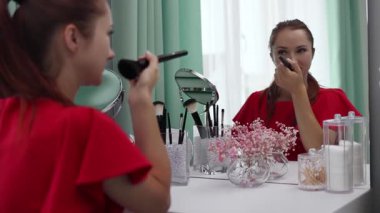 Gece elbisesi giymiş bir kız yüzüne pudra sürer. Genç ve çekici bir kadın makyaj yapıyor. Tuvalet masasının arkasında..