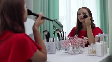 Gece elbisesi giymiş bir kız yüzüne pudra sürer. Genç ve çekici bir kadın makyaj yapıyor. Tuvalet masasının arkasında..