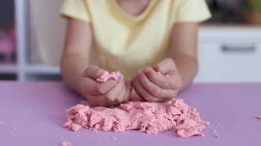 Çocuk kinetik kumla oynuyor ve yavaş çekimde elinde karıştırıyor. Pembe kinetik anti-stres kumu olan çocukların ellerine yakından bakın. Çocuklar ve yetişkinler için stres önleyici oyuncak.