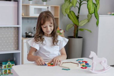 Küçük kız çocuk odasındaki masada masa eğitimi üzerine oyun oynuyordu. Çocuk gelişimi kavramı. Çocuklar için boş zaman kavramı..