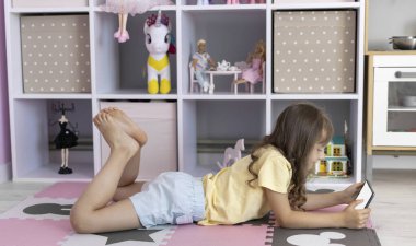 Tablet kullanan Avrupalı görünümlü küçük bir kız. Çocuk sanal oyunlar oynuyor ya da tabletinde çizgi film izliyor. Tabletli çocuk. Alet bağımlılığı sorunu..