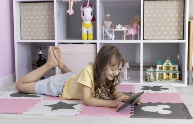Tablet kullanan Avrupalı görünümlü küçük bir kız. Çocuk sanal oyunlar oynuyor ya da tabletinde çizgi film izliyor. Tabletli çocuk. Alet bağımlılığı sorunu..