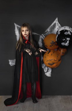 Cadılar Bayramı 'nda siyah ve kırmızı bir kostüm giyen küçük bir kız siyah bir arka planda örümcek ağlarıyla izole edilir. Cadılar Bayramı konsepti.