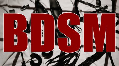 BDSM inscription on background of sex toys for submission and domination with erotic role-playing games. Creative concept with leather whip, handcuffs and mask