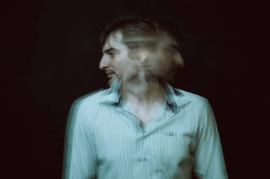 schizophrenic portrait of psychopathic man with mental disorders in white shirt on dark background