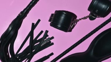 set of adult erotic toys for BDSM sex with submission and domination. Leather flogger whip, handcuffs, mask on pink background