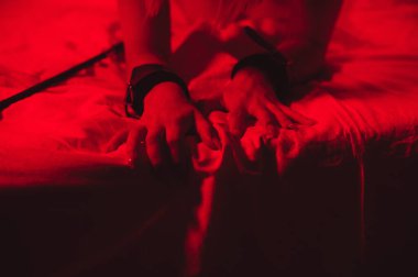 girl hands in handcuffs and leather whip flogger for BDSM sex with submission and domination lie on bed in bedroom