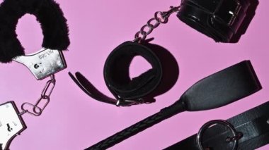 Handcuffs, whip flogger for BDSM sex with submission and domination. A set of adult intimate erotic sex toys on a pink background