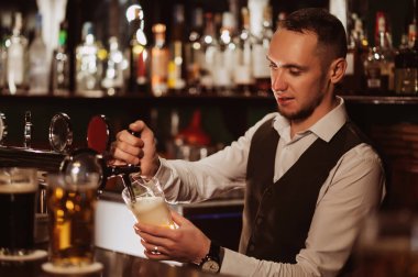 Barmen barın arkasındaki barın musluğundan bardağa bira doldurur.