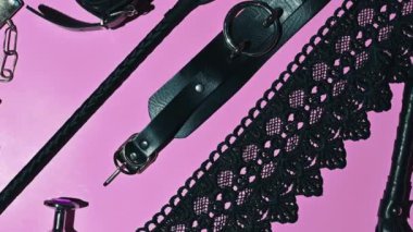 set of adult erotic toys for BDSM sex with submission and domination. Leather flogger whip, handcuffs, mask on pink background