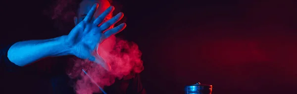 male smoker smokes a hookah in a shisha bar and lets out a cloud of smoke putting his hand forward on a dark background
