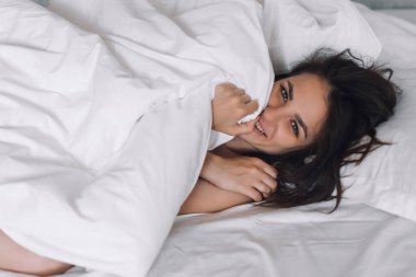 Yatak odasındaki battaniyenin altında yatan seksi, çıplak esmer bir kızın portresi.