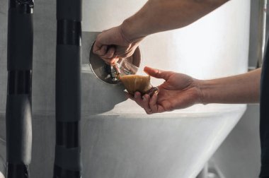 Bira fabrikasındaki bira imalatçısı teftiş için depodan bir bardağa bira doldurur.