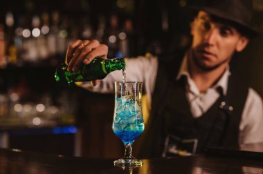 Barmen, bardakta mavi lagün kokteyli ile bir restoranın barındaki buzu karıştırıyor.