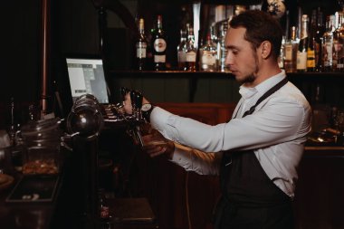 Bardaki barmen fıçıdan gelen muslukla bardağa bira doldurur.