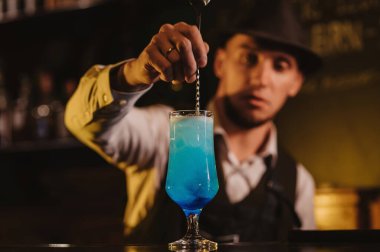 Barmen, bardakta mavi lagün kokteyli ile bir restoranın barındaki buzu karıştırıyor.