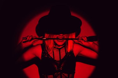 İç çamaşırlı ve şapkalı seksi kız dişlerinde kırbaç tutuyor. Baskın kadın BDSM konsepti