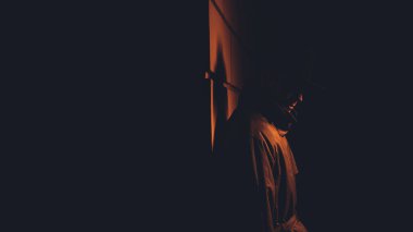 Siyah film tarzında gece vakti şapkalı ve yağmurluklu bir erkek mafya dedektifi.