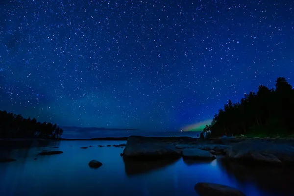 stock image night landscape with a starry sky and Milky way with many bright stars. Astrophotography with constellations and galaxies over water of a lake with rocks and a forest on background