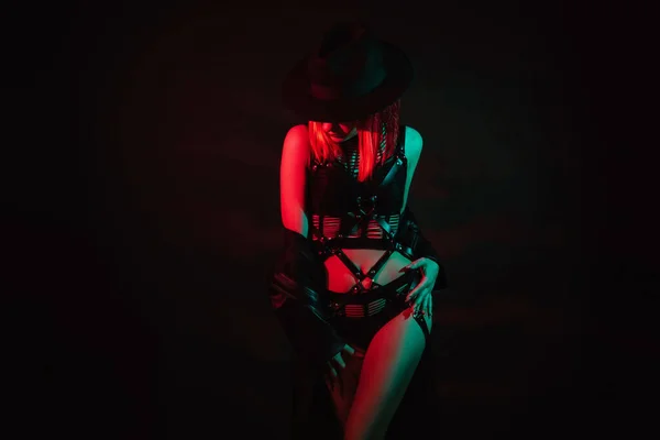 穿着漂亮内衣裤 皮带和帽子的性感女孩穿着漂亮的女装 背景是黑色的霓虹灯 — 图库照片